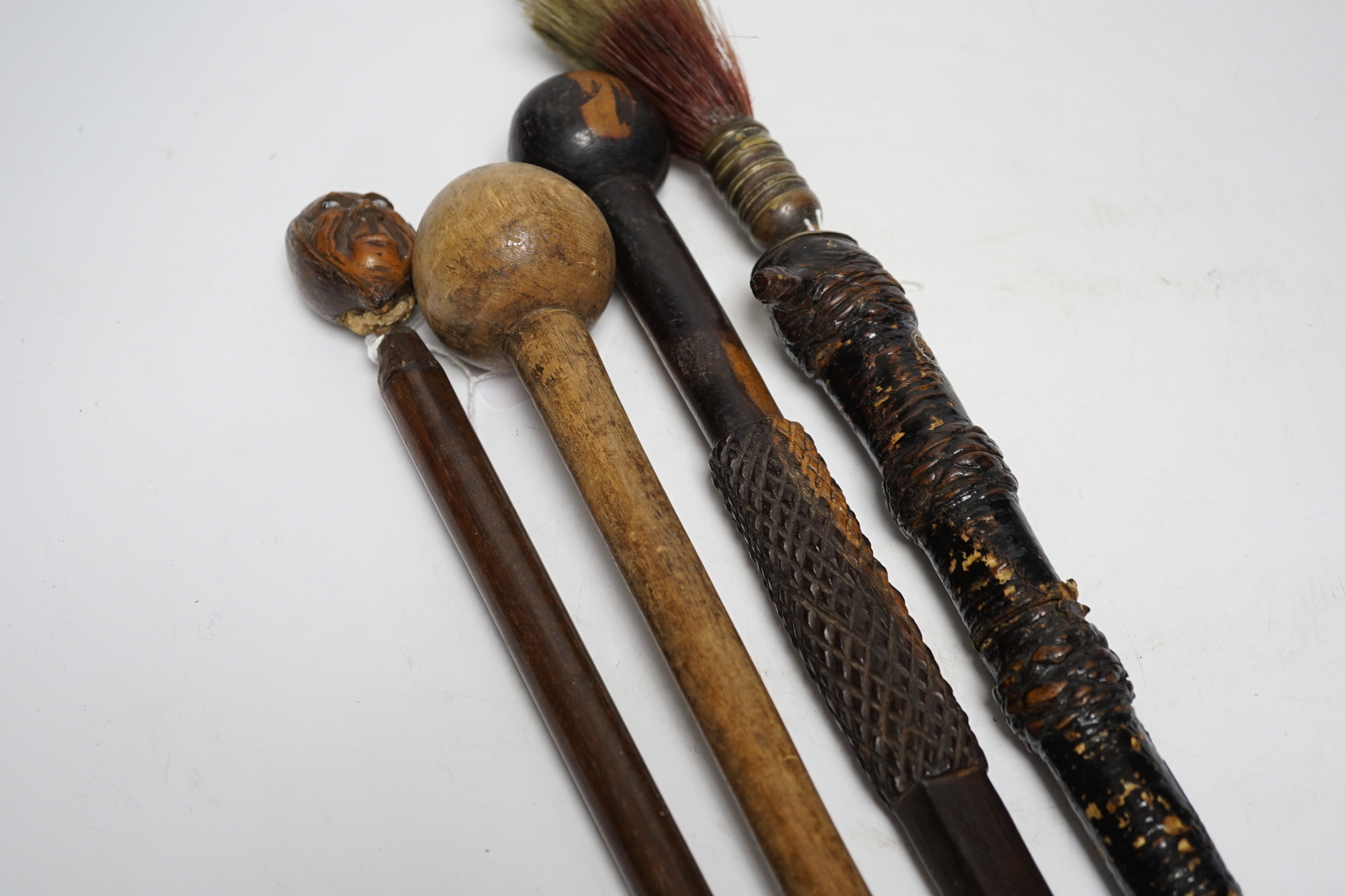 A ceremonial sword stick with removable brush end, a 19th century continental carved head with glass eyes on associated cane stick and two others, longest 93cm